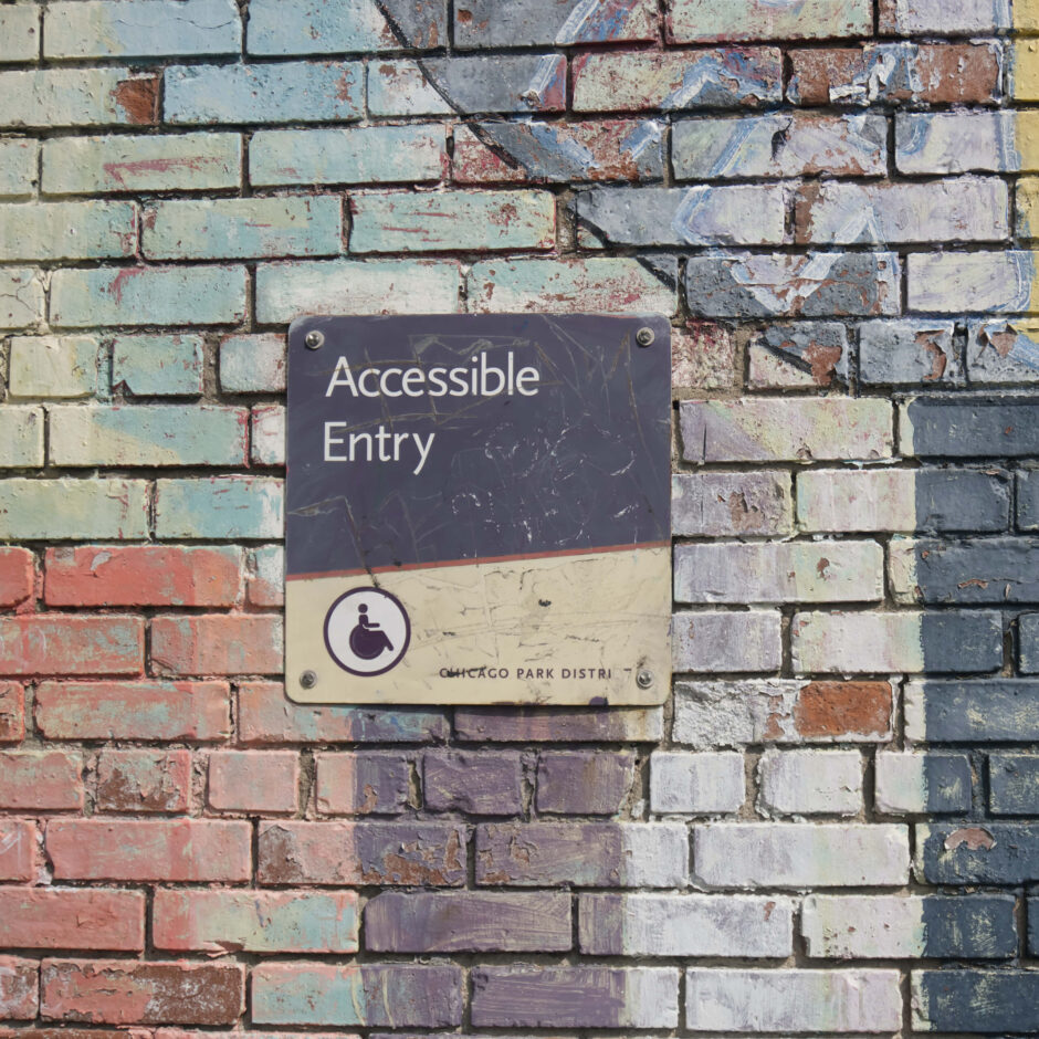 A wall painted in many colours with a sign saying ' Accessible Entry' with a stylised picture of a person in a wheelchair.