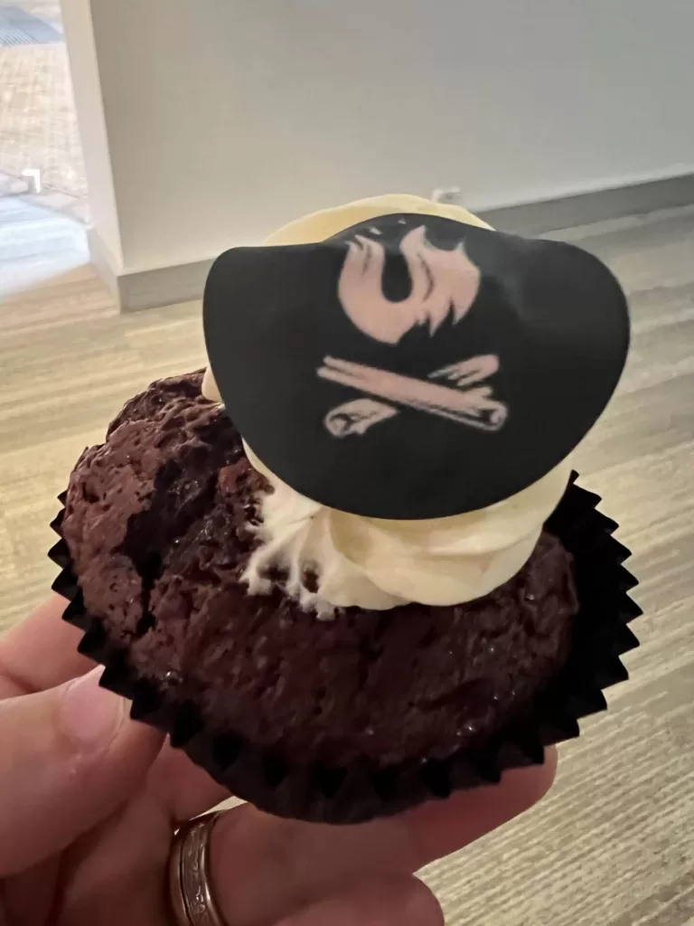 A photo of one of the fantastic cupcakes provided for afternoon tea. It is a chocolate cupcake with a dollop of cream and an edible paper UX Camp logo on top.
